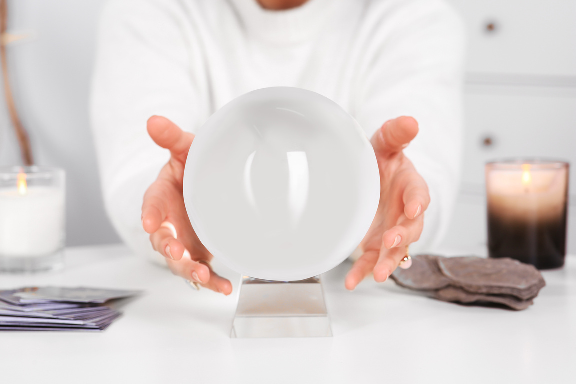 Soothsayer Using Crystal Ball to Predict Future at Table Indoors